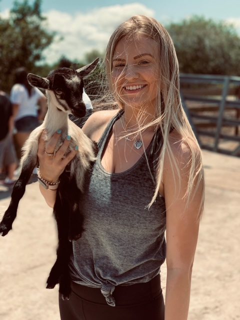 Abbi smiling brightly while holding a baby goat — pure joy