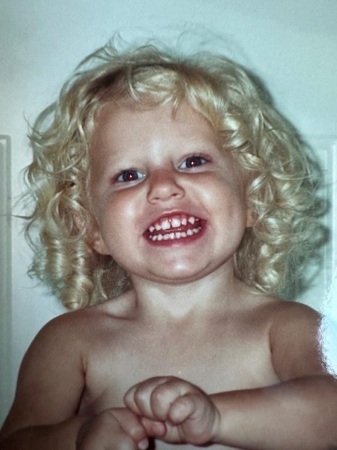 Abbi as a curly-haired toddler with the brightest smile