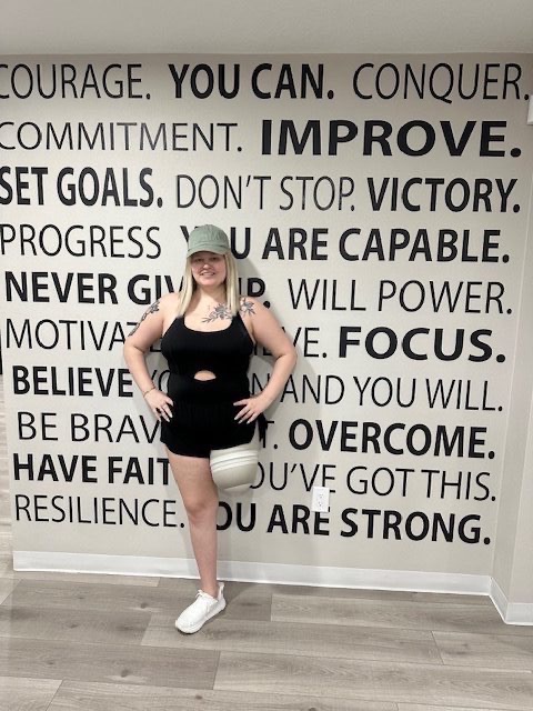 Abbi standing in front of a motivational quote wall — strong