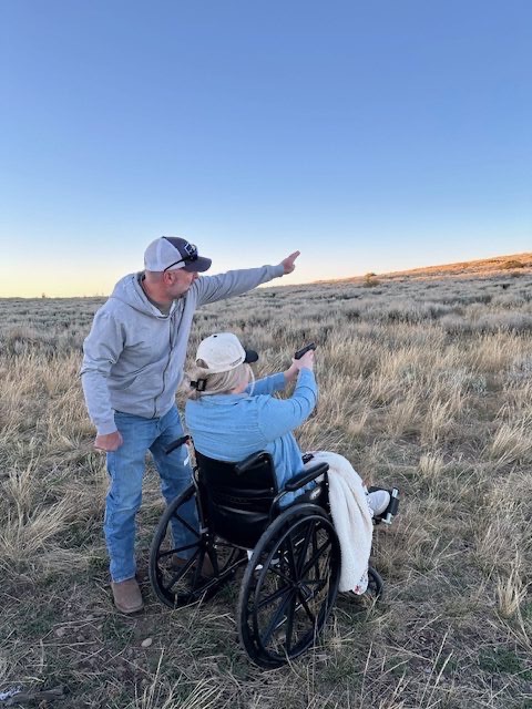 Abbi in a wheelchair with her dad pointing at the horizon at sunset