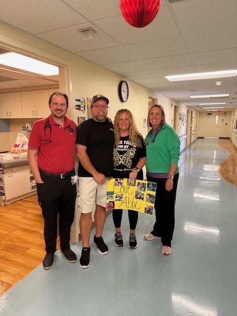 Family with hospital staff in pediatric hallway holding Love Abbi sign